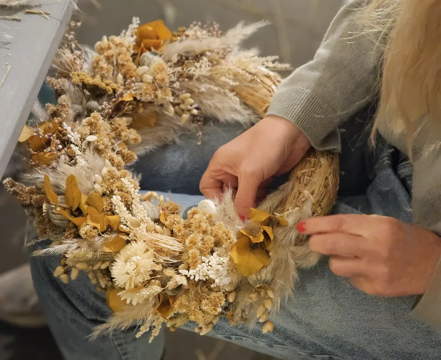 Person crafting dried flower wreath indoors.