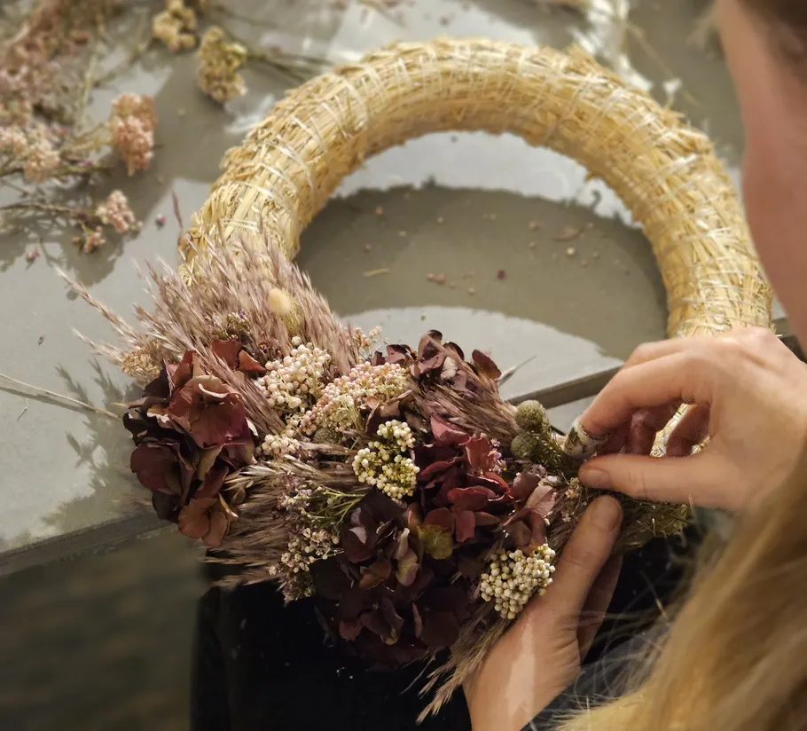 Person arranging flowers on a straw wreath.