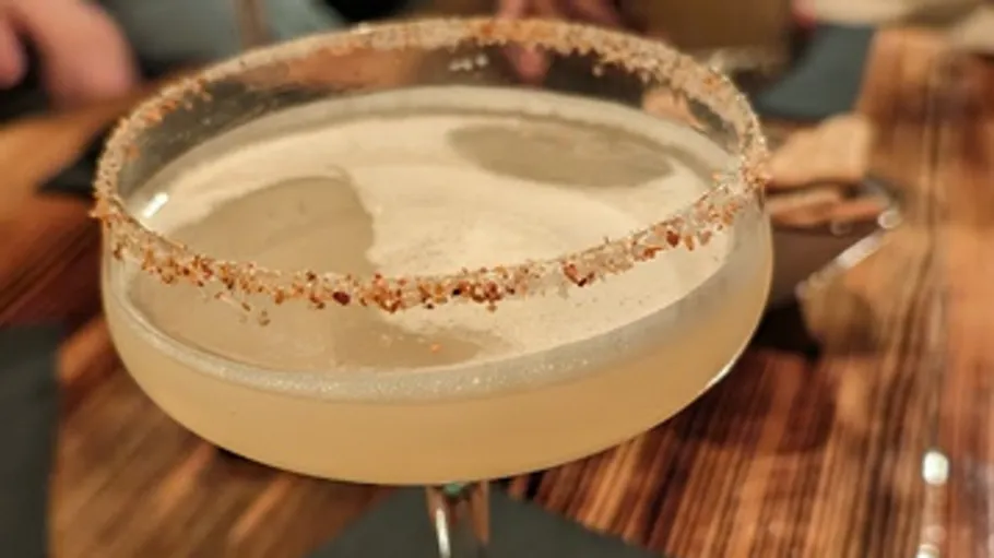 Cocktail glass with salted rim on table.