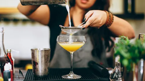 Barkeeper gießt Cocktail durch Sieb ins Glas.