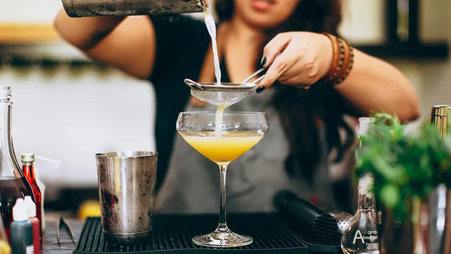 Bartender pours cocktail through strainer into glass.