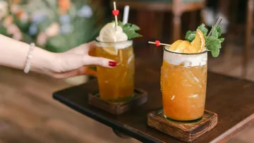 Hands placing cocktails on a wooden table.