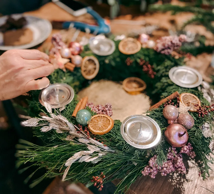 Hand decorates Christmas wreath on wooden table.