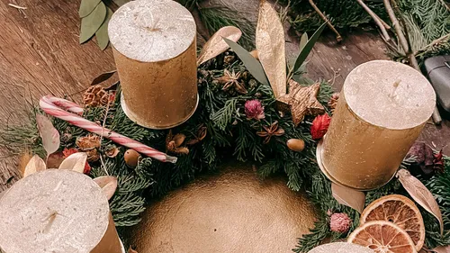 Goldene Kerzen auf einem dekorierten Adventskranz.