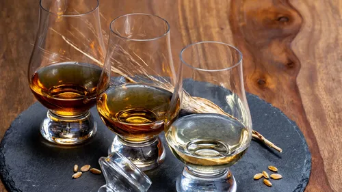 Three whiskey glasses on slate plate, wooden table.