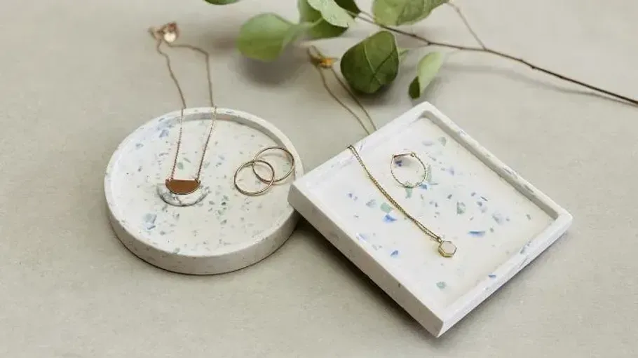 Schmuck auf Terrazzo-Schalen mit grünen Blättern.