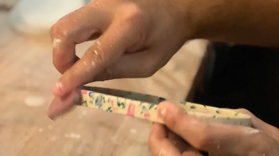 Hands sanding multicolored material on wooden table.