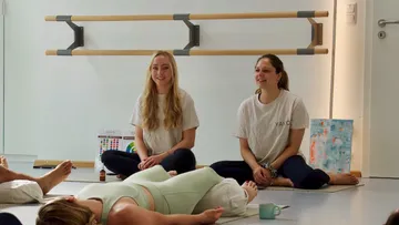 Zwei Frauen leiten einen Yoga-Kurs drinnen.