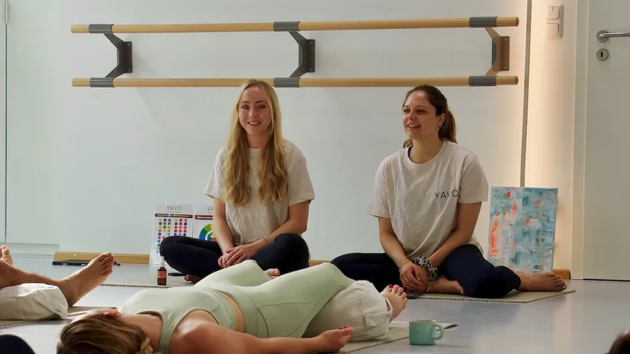 Zwei Frauen leiten einen Yoga-Kurs drinnen.