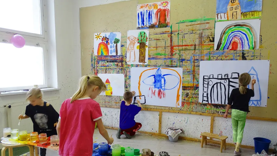 Kinder malen bunte Wandbilder drinnen.