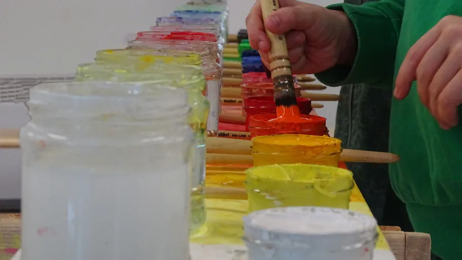Hand dips paintbrush into colorful paint jars.