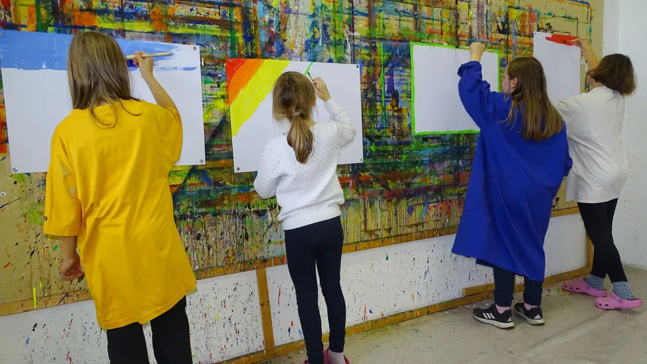 Four children painting on large art wall.