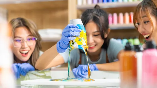 Three people pouring colorful paint excitedly.
