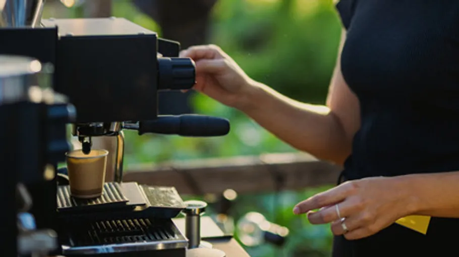 Person macht Kaffee mit Espressomaschine im Freien.