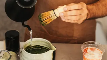 Person preparing matcha tea with whisk.