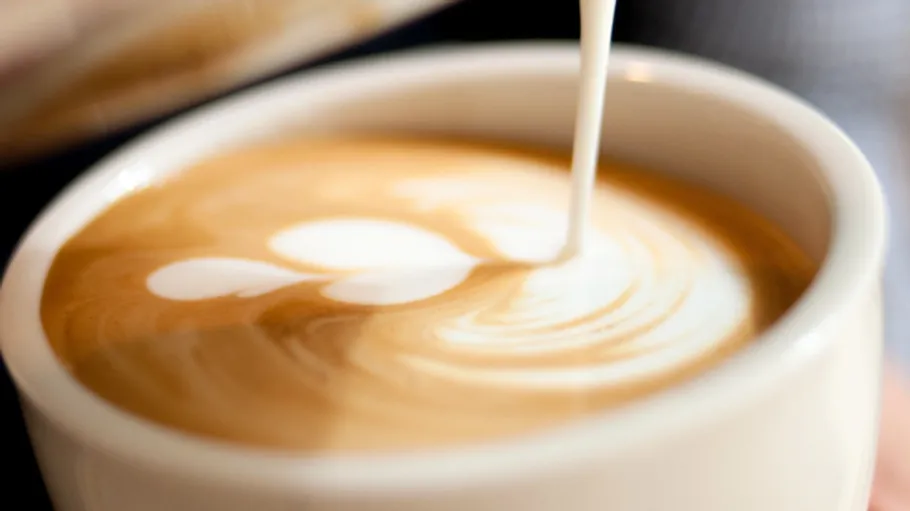 Coffee cup, latte art being poured.