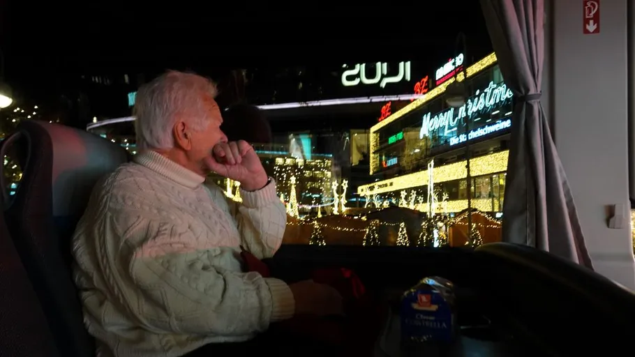 Man on bus looks at festive city lights.