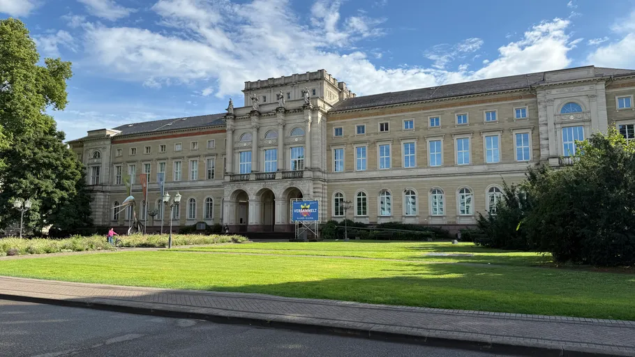 Historisches Gebäude mit Rundbogenfenstern, üppiges Grün.