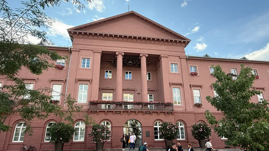 Rotes Gebäude mit Säulen und Menschen davor.