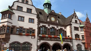 Historisches Gebäude mit Uhr und Flaggen, belebte Straße.