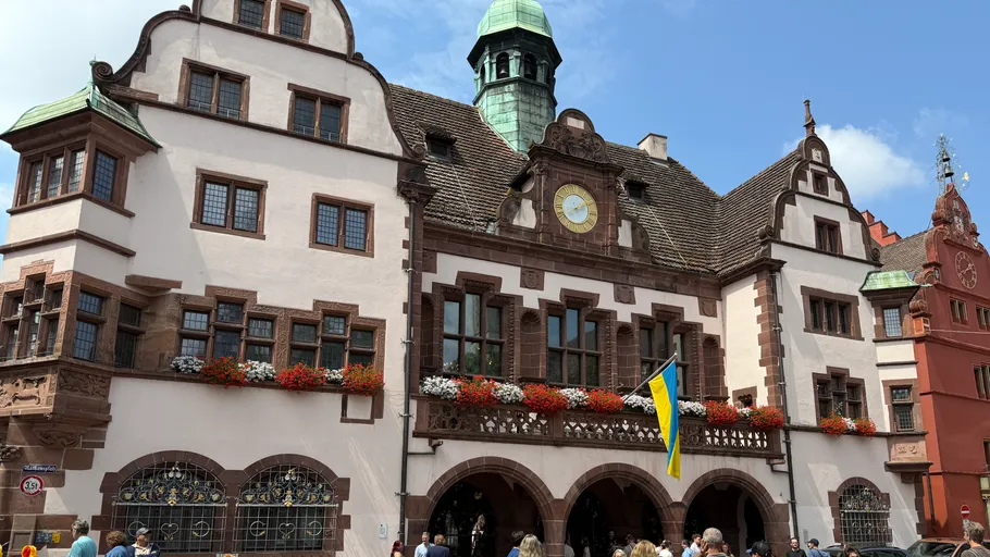 Historic building with clock and flags, crowded street.