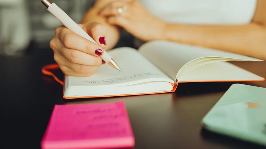 Hand schreibt in Notizbuch auf Schreibtisch.
