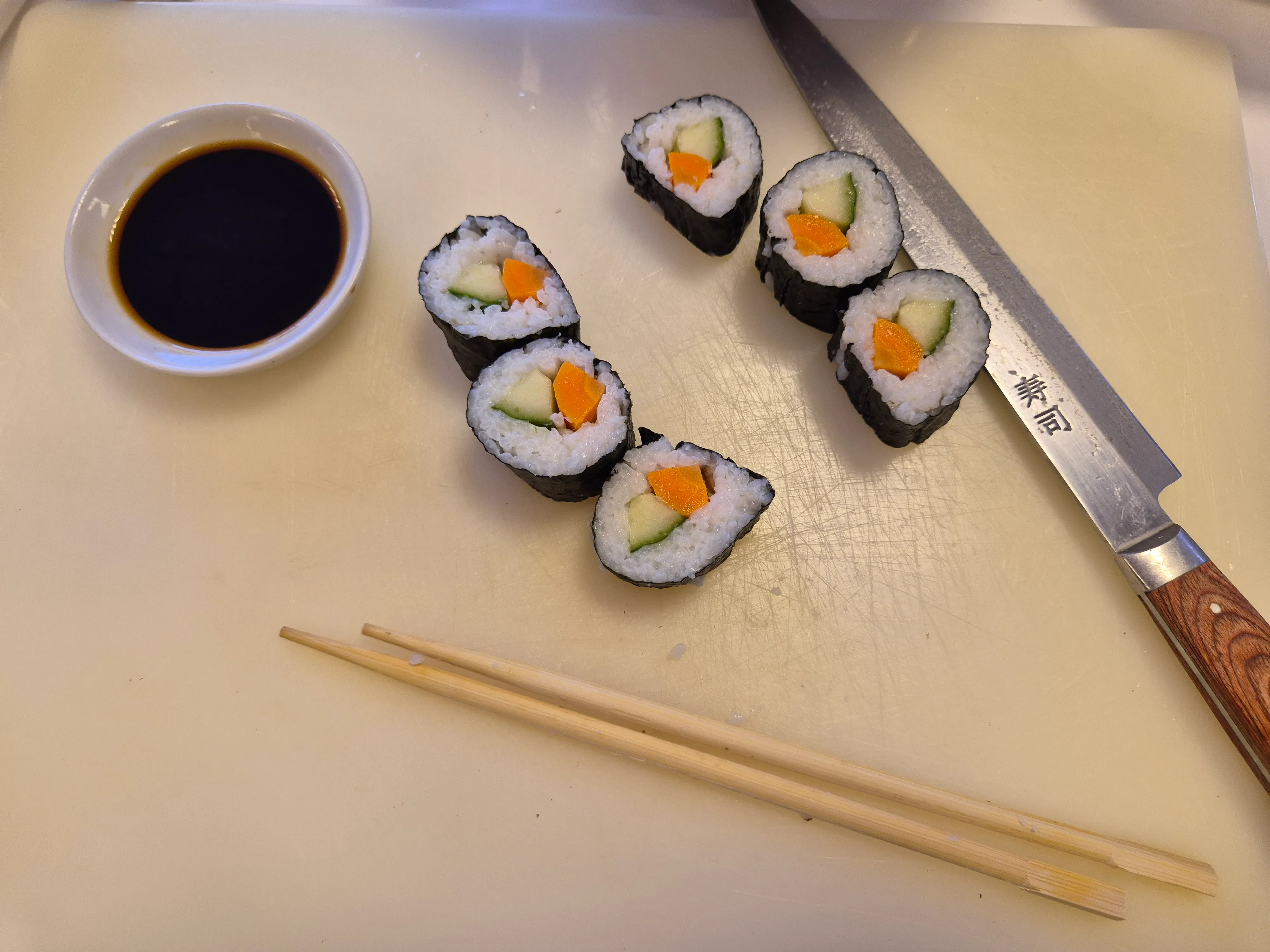 Sushirollen, Messer, Sojasauce und Stäbchen auf Brett.