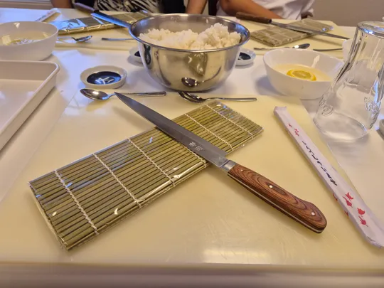 Tisch mit Sushi-Matte, Messer und Schüsseln gedeckt.