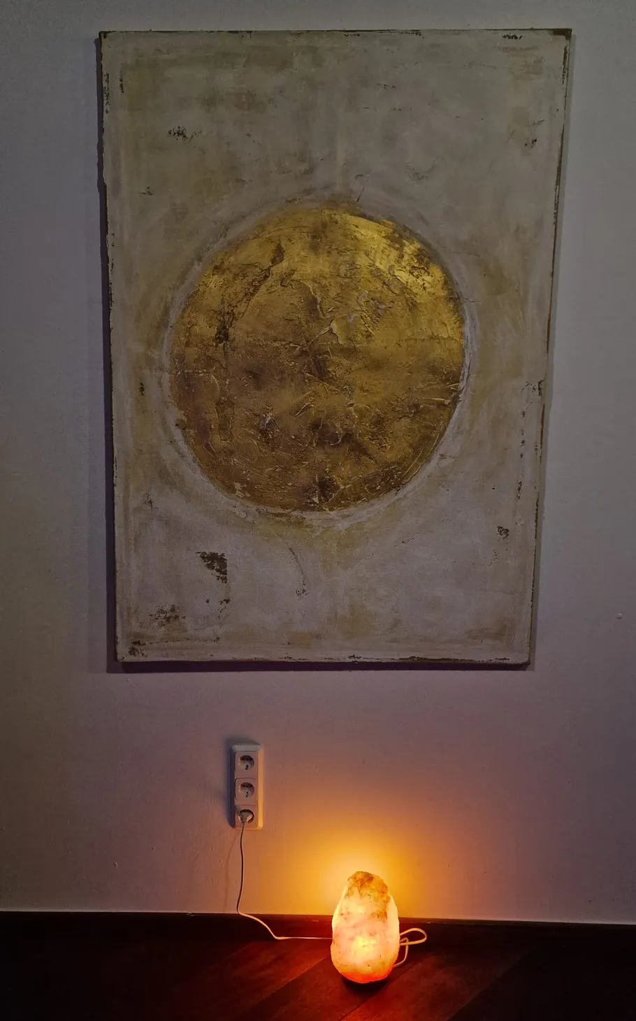 Abstraktes Gemälde und Salzkristalllampe an Wand.