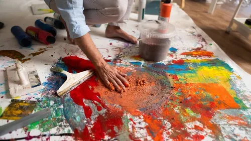 Person mischt bunte Farben auf dem Boden.