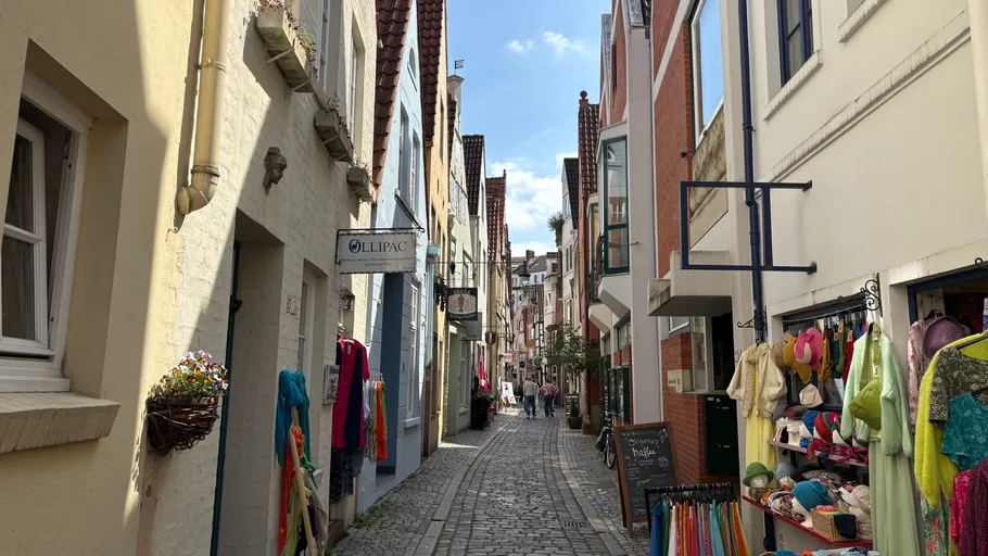 Narrow cobblestone street with colorful clothing shops.
