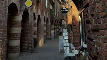 Schmale Ziegelgasse mit Geschäftsschildern.