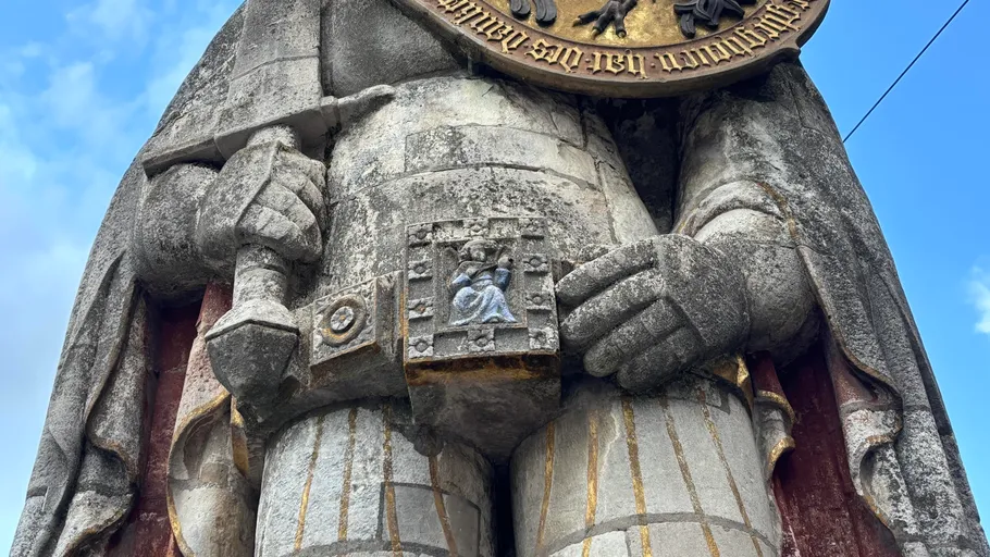 Steinstatue hält Schild und Schwert im Freien.