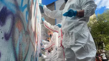 People in suits spray-painting a wall outdoors.