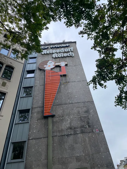 Großes Schild an Gebäudewand, von Bäumen umgeben.