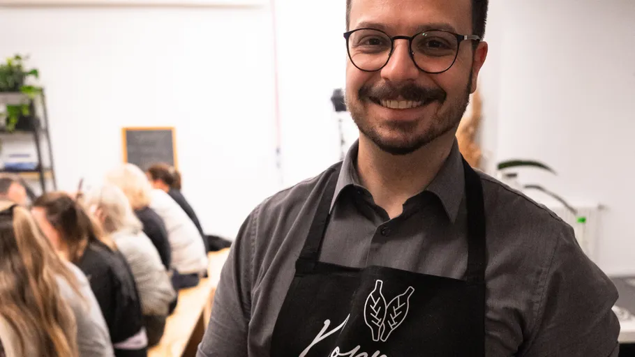 Man smiling wearing apron, people seated behind.