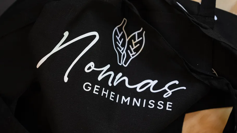 Schwarze Schürze mit 'Nonnas Geheimnisse' und Blättern.