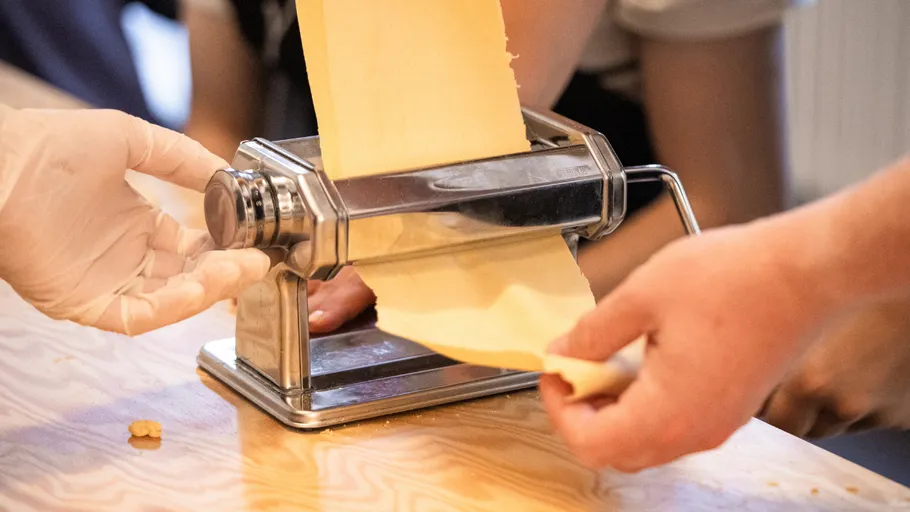 Hände benutzen Nudelmaschine auf Tisch.
