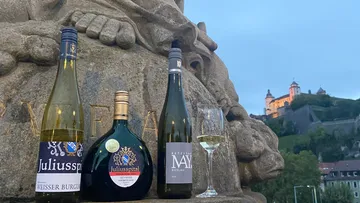 Weinflaschen und Glas auf Steinbank, Burg im Hintergrund.