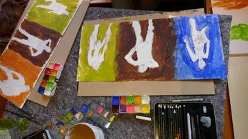 Art supplies on table with colorful paintings.