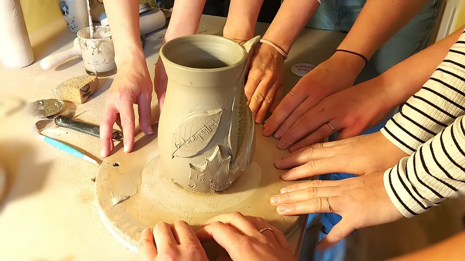 Hands crafting clay pot on spinning wheel.