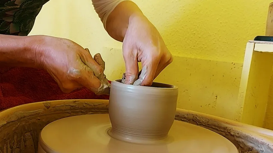 Hands shaping pottery on spinning wheel.