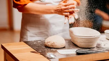 Person bereitet Teig auf Holztisch vor.