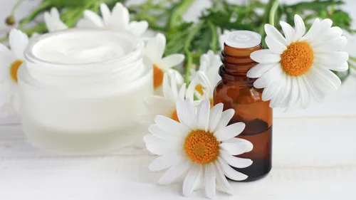 Glas und Flasche mit Gänseblümchen auf Tisch.