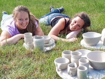 Two women lie in the grass next to ceramic crockery.