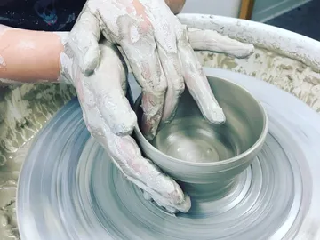 Pottery hands form a bowl-shaped ceramic on a turntable.