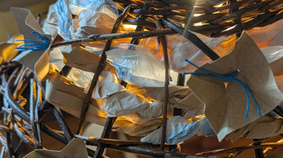 Geflochtener Lampenschirm mit Papier und blauen Bändern.