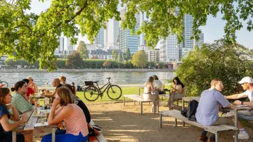 People eating at outdoor tables by river.