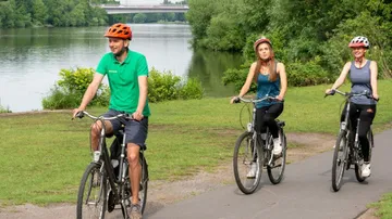 Three people cycling near a riverside pathway.