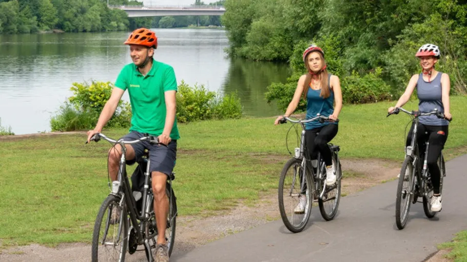 Drei Personen radeln am Flussufer entlang.